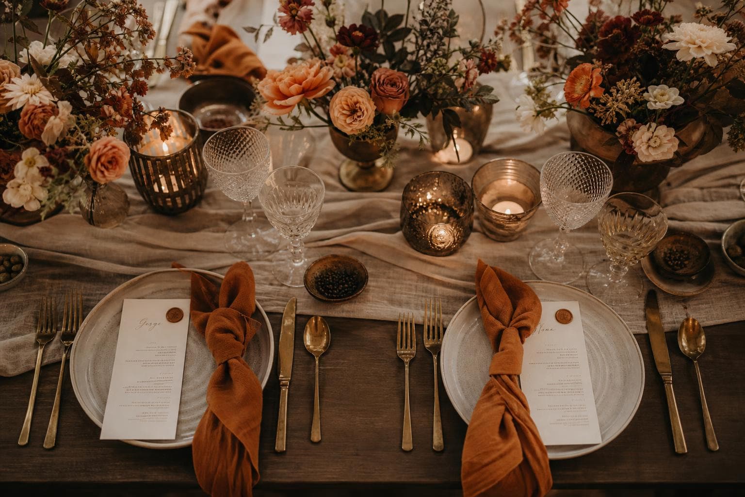 A tablescape concept with warm-toned flowers, candles and table linens